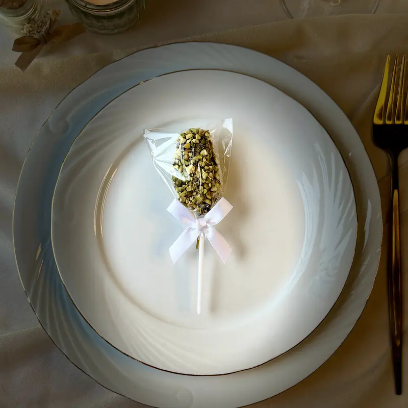 Sucette de dattes à la pistache, nœud satiné, posée au centre de l’assiette d’un invité