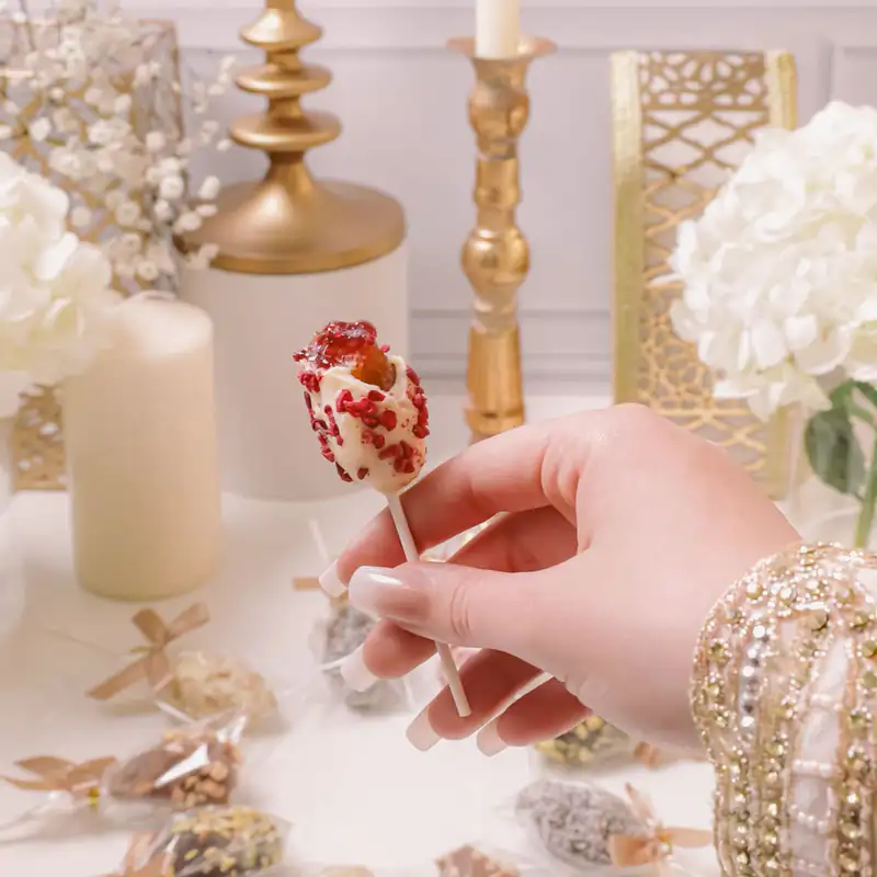 Une invitée tient une sucette de dattes à la framboise devant une table de mariage dressée